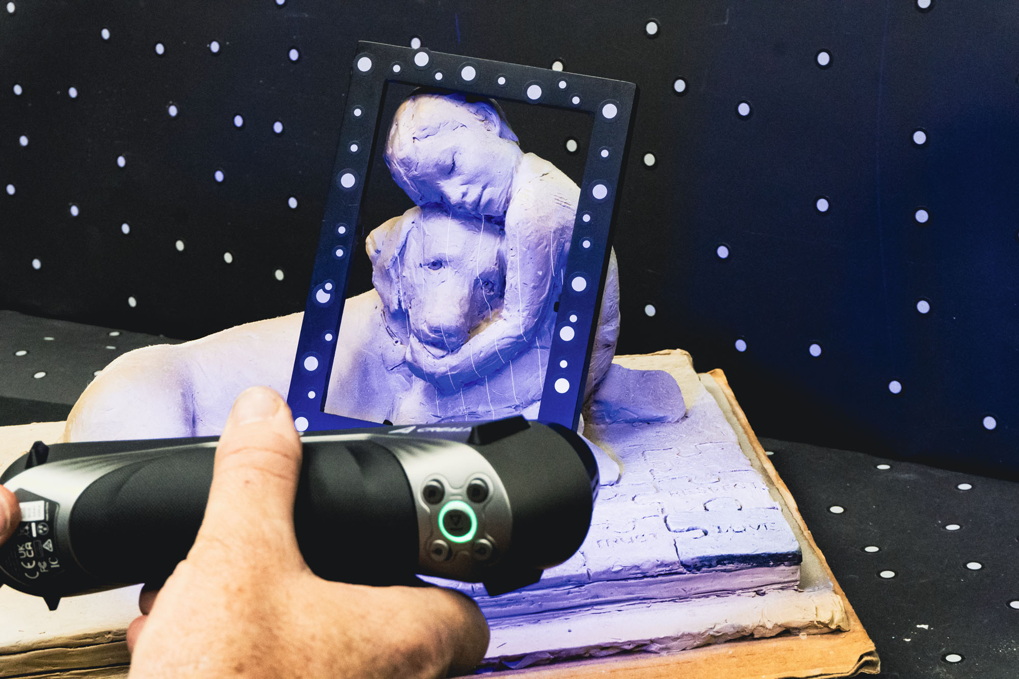 A person using a handheld 3D scanner to capture a digital model of a sculpture depicting a mother holding a child.