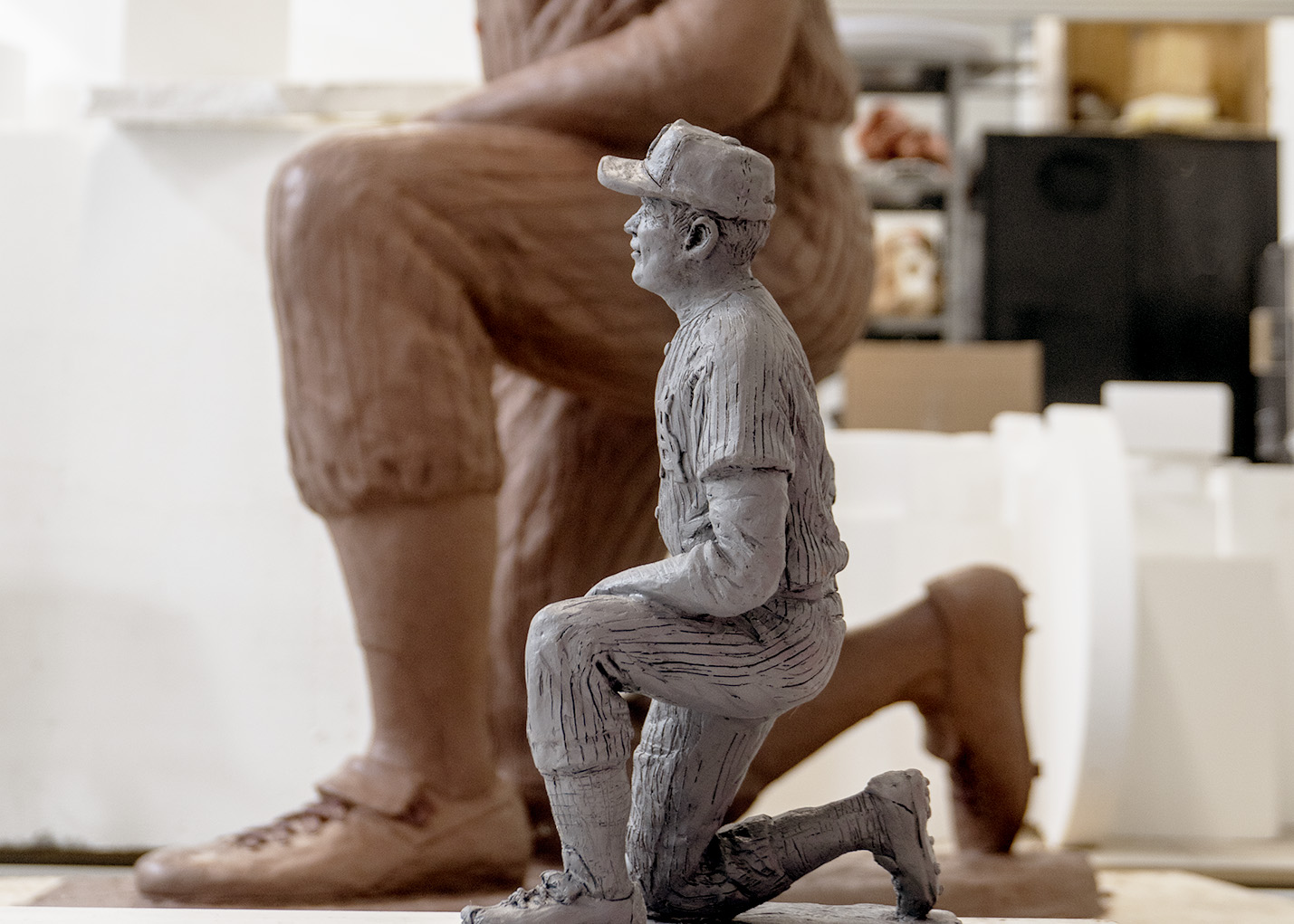 A small artist's maquette in clay sits next to a sculpture enlargement that has been modified by the artist with a layer of clay. 
