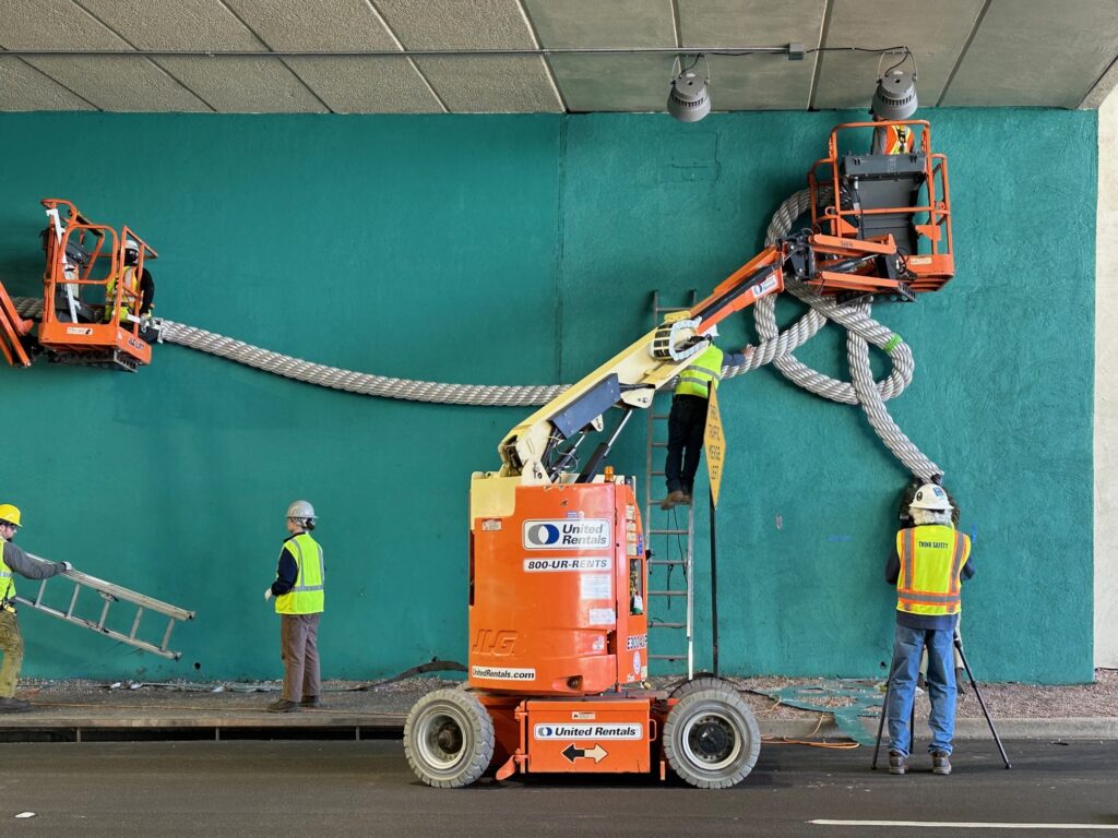 The teal installing Breakaway, on a teal painted wall wearing high-vis vests.