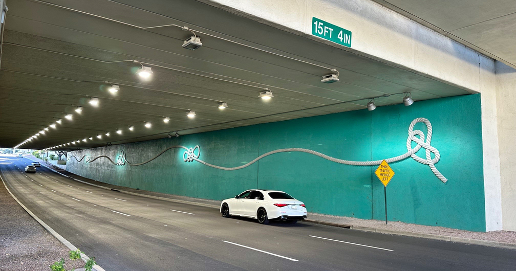 Completed installation of Barbara Grygutis’ Breakaway on a teal-painted wall of the underpass, a car is shown driving under the installation.