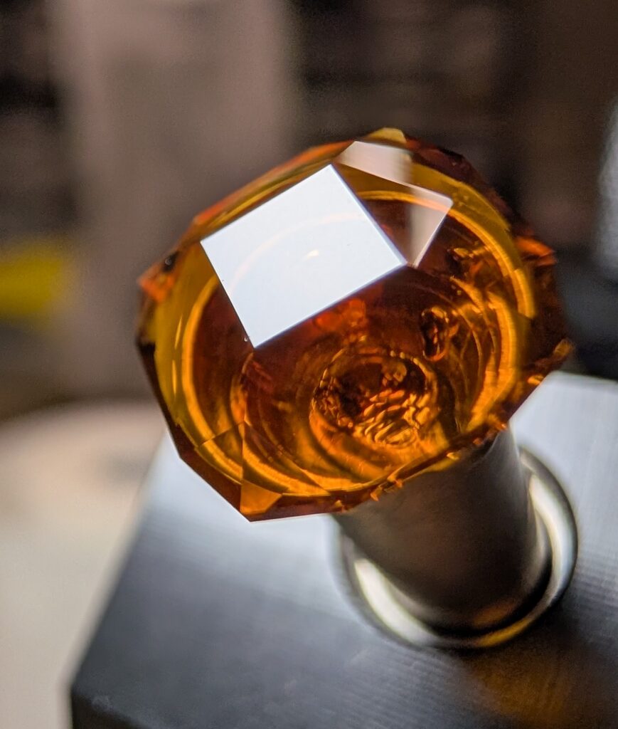 A dark orange gemstone on a dop being faceted by James
