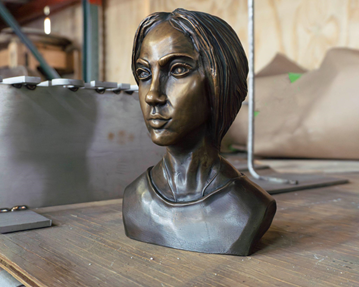 The completed sculpture sits on a wooden shelf in the workshop, the lighter brown areas reflecting the ambient light.